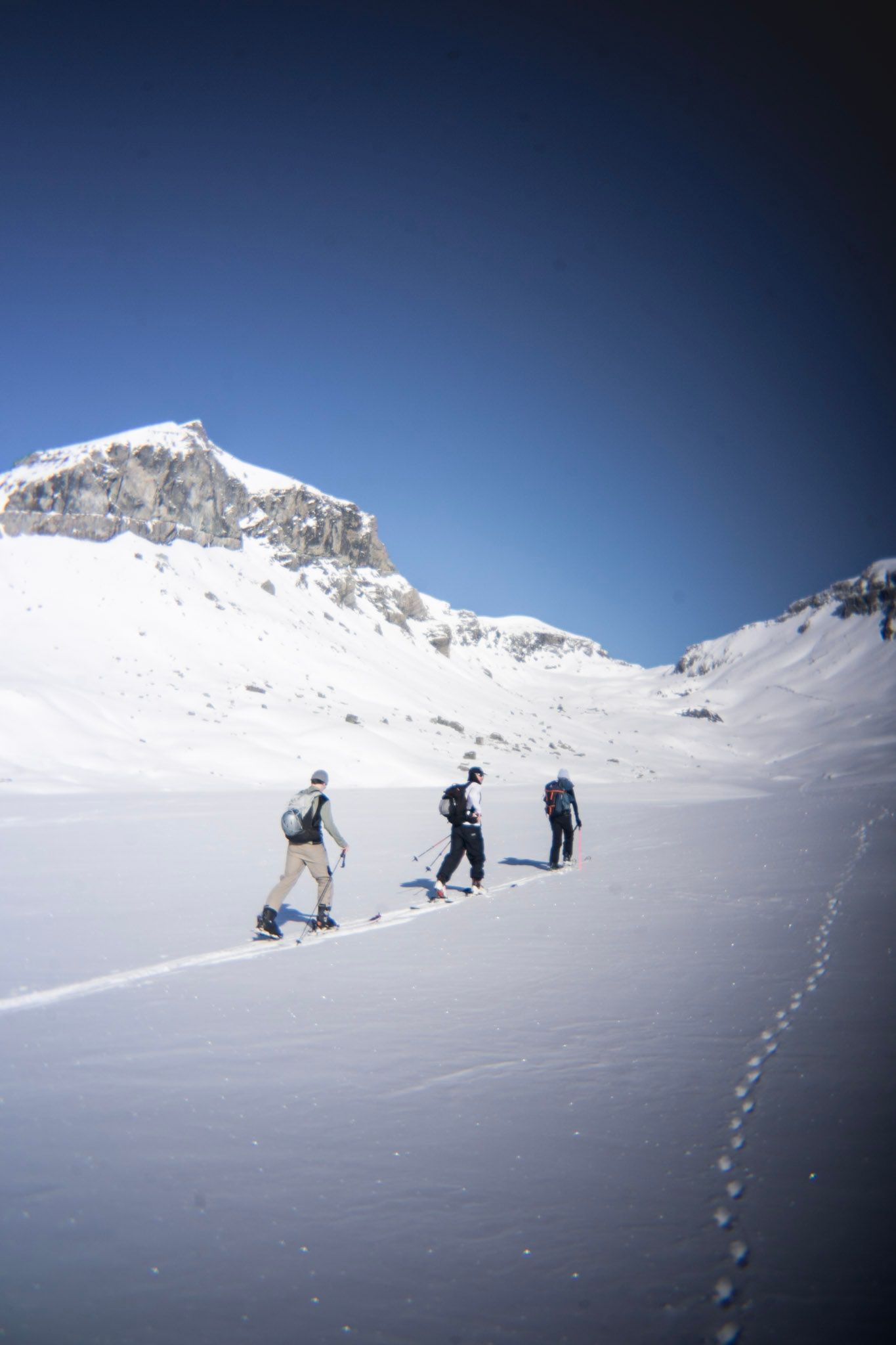 Drei Freerider gehen im Schnee auf einen felsigen Gipfel zu