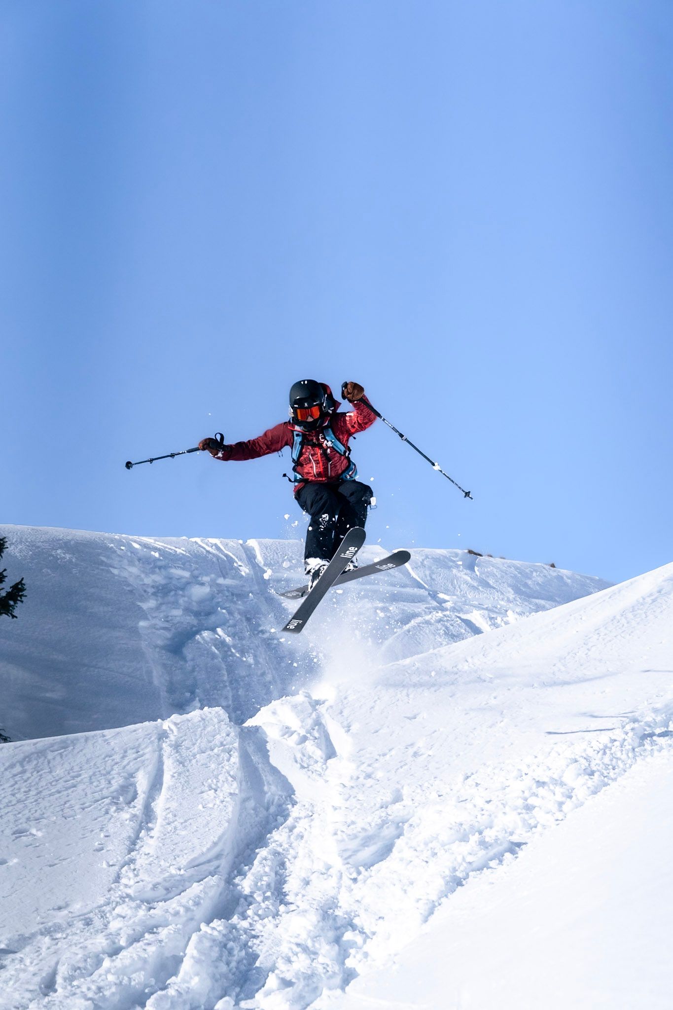 Skifahrer in roter Jacke springt über eine Schneekante vor blauem Himmel