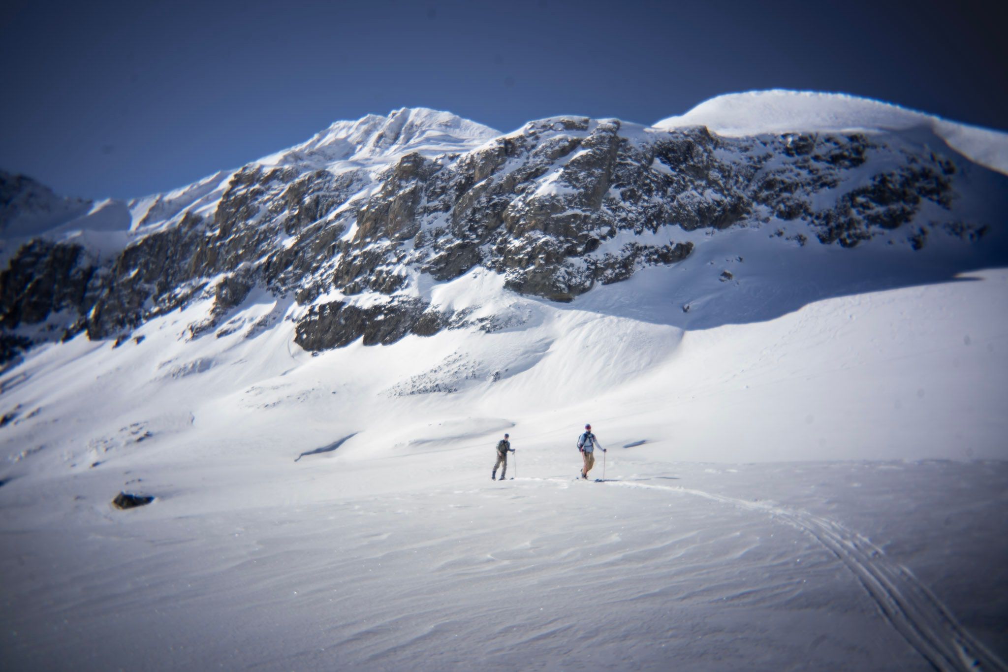 Zwei Skitourengeher steigen unter einer mächtigen Felswand auf